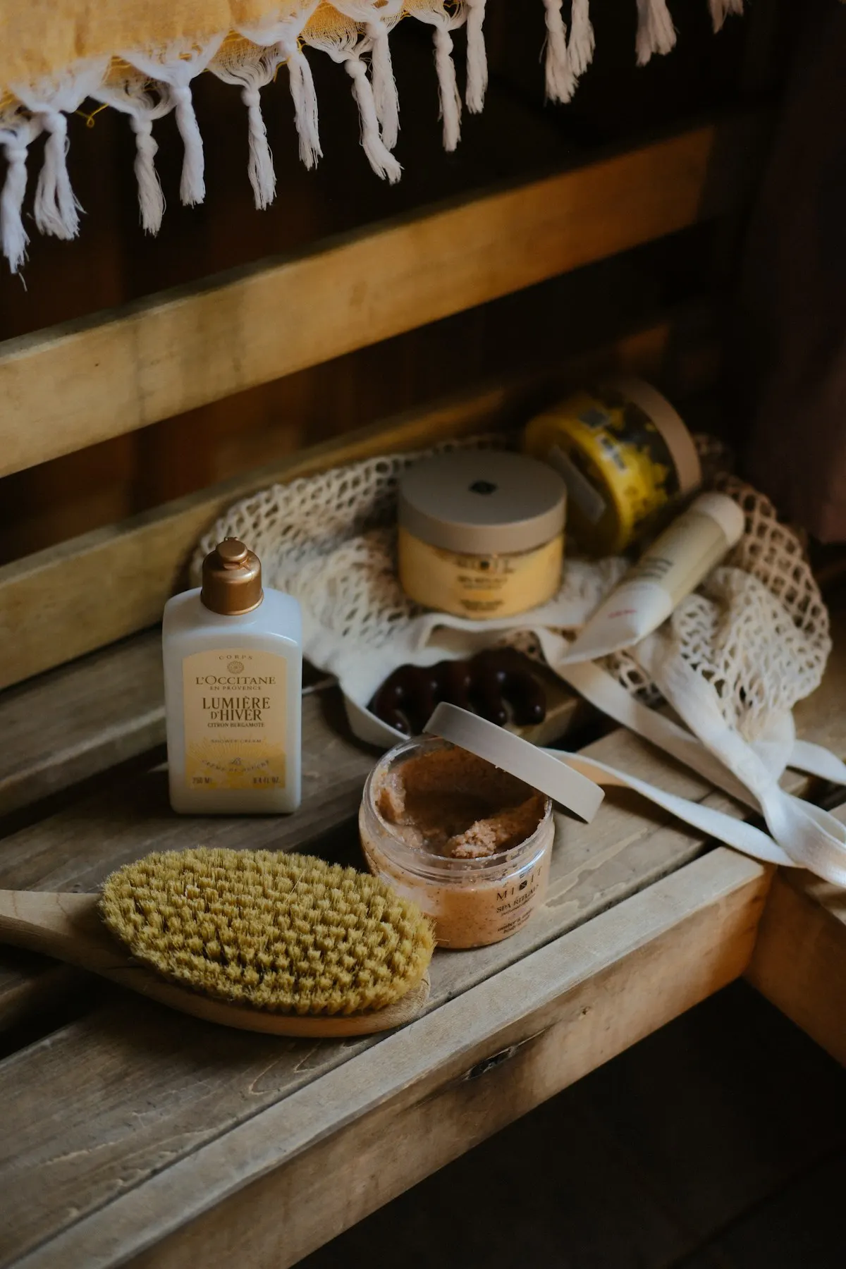 Body scrub jars and a natural bristle body brush on a wooden bench