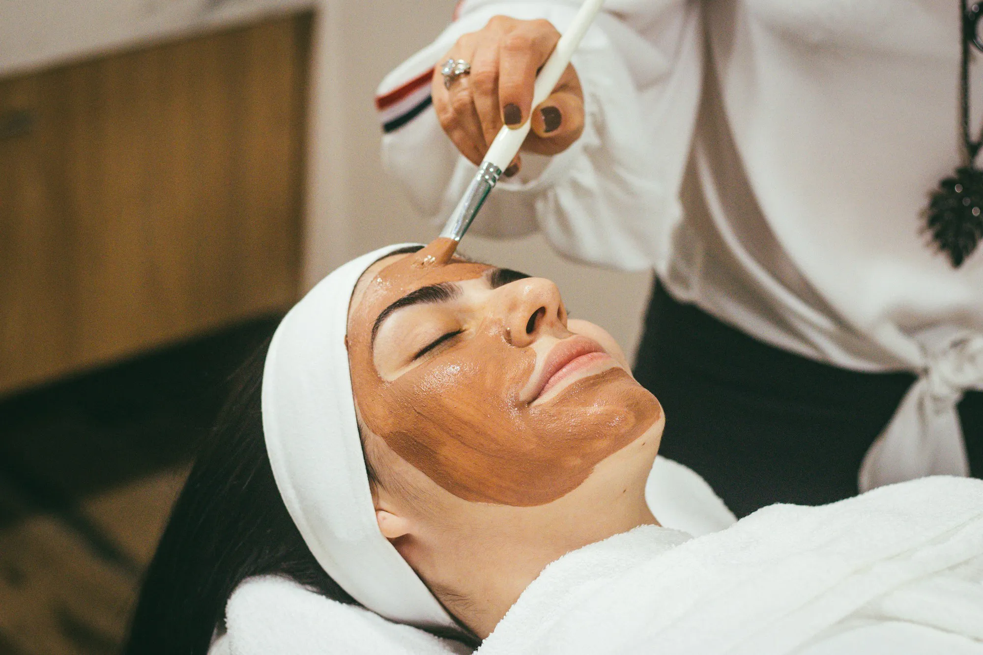 A therapist brushes a clay mask onto a guest's face during a facial